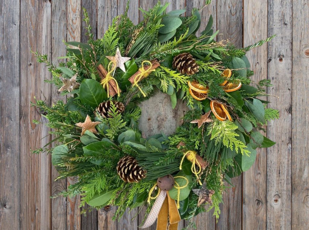 A lush green wreath filled with gold stars, orange ribbon, dried orange slices, and pine cones.