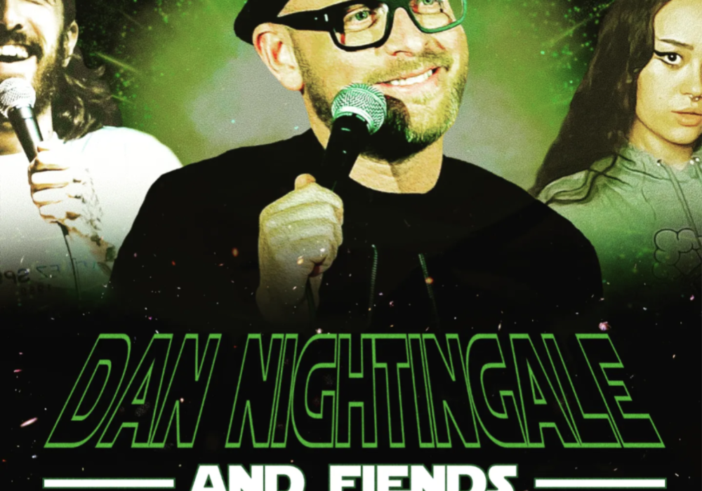 A green tinged photo of comedian Dan Nightingale, he is holding a microphone and smiling. He is flanked by two other comedians.