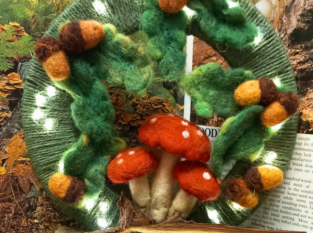 A green felted hoop, covered in acorns and toadstools, dotted with fairy lights.