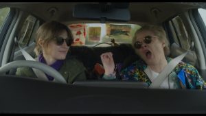 Two women in a car both in sunglasses, one singing