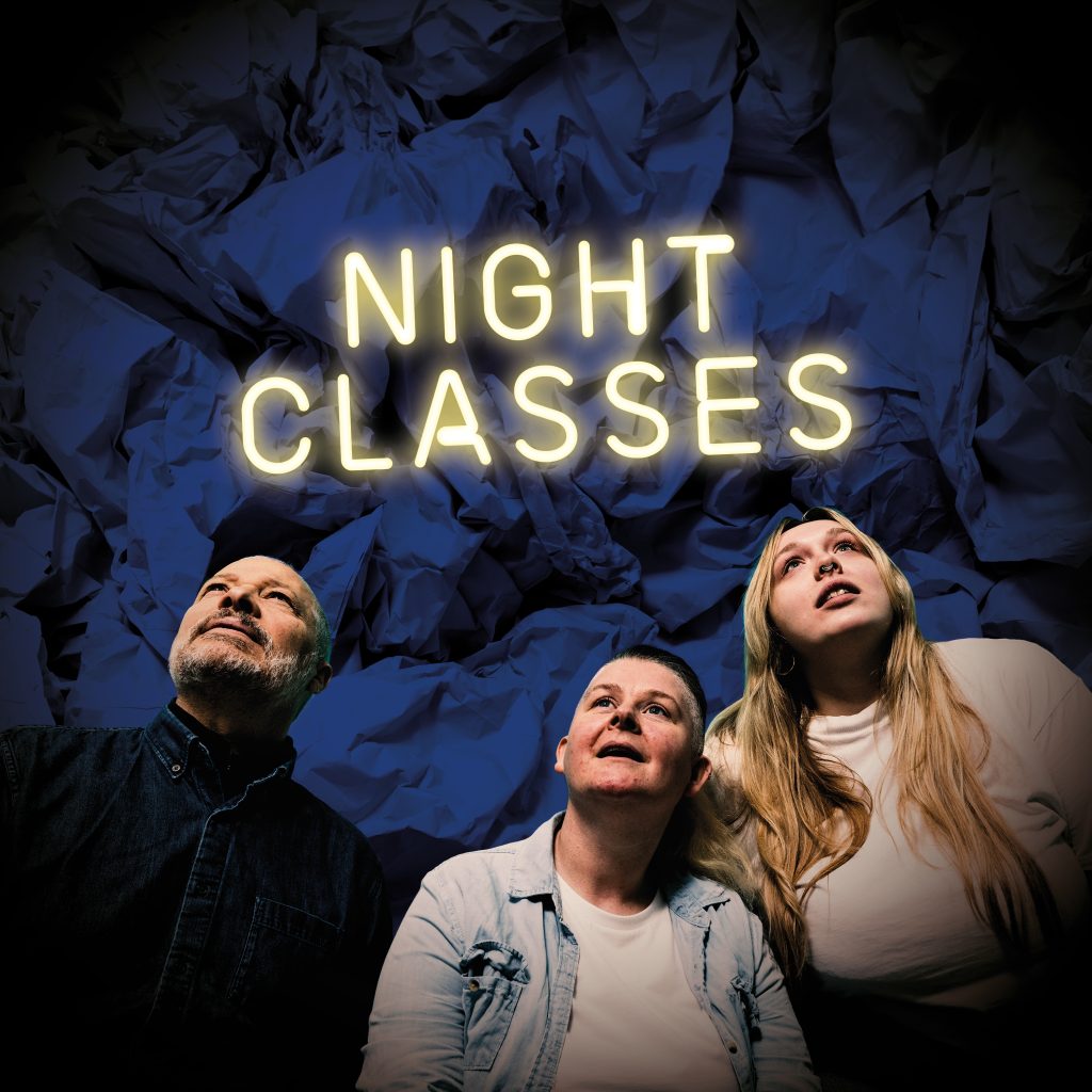 Three people looking upwards at a neon sign saying NIGHT CLASSES
