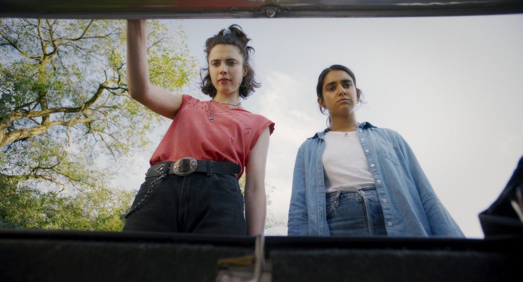 Image of Margaret Qualley wearing a pink T-shirt and Geraldine Viswanathan in a white t-shirt and blue overshirt looking down towards the camera which is positioned at a low andgle.