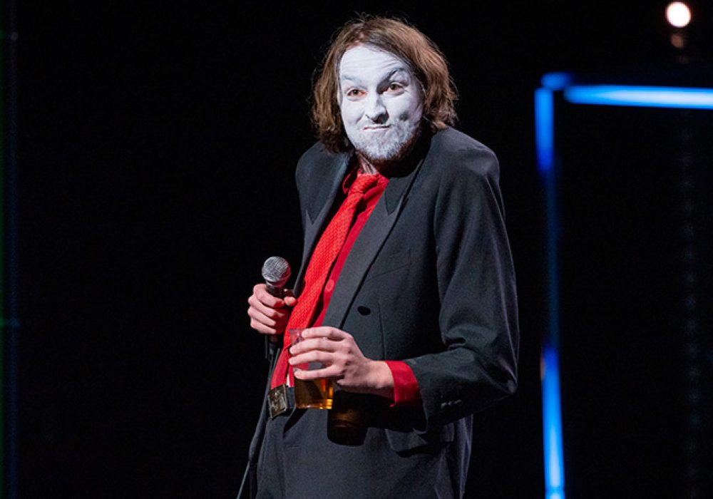 An image of Joe Kent-Walters on stage, wearing thick white stage make-up on their face.