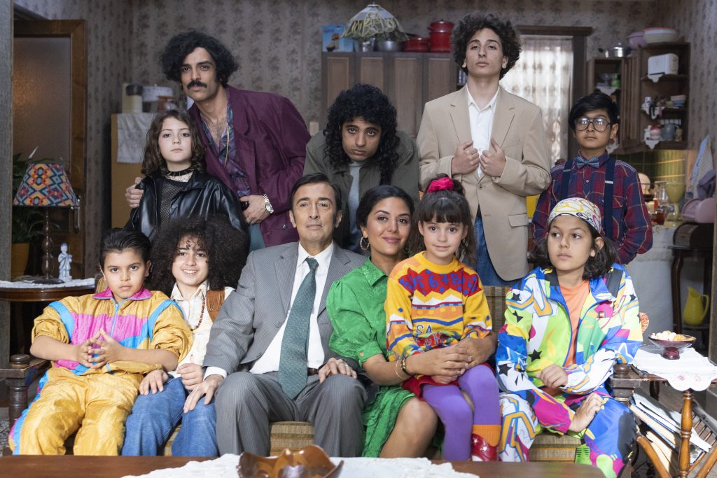 The main characters of the story, A large Iranian-american family look directly into a camera taking a family photo.