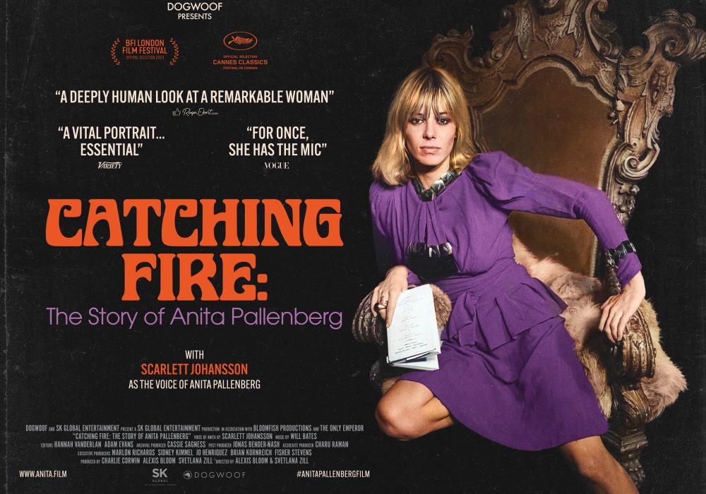 Catching Fire in Orange text with a white female with blonde hair in a long bob style with a fringe. She is wearing a long-sleeved purple long sleeved dress. She has one knee on an arm chair and one on the floor.