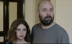A father and daughter. Male, white, bald with black/grey beard wearing a grey t-shirt, daughter white with mid-length brown hair.