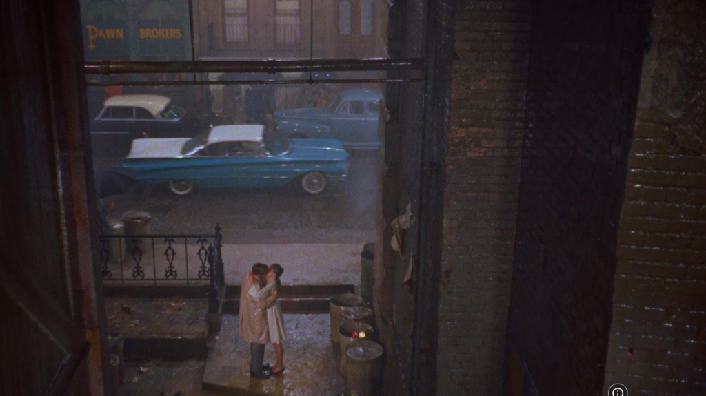 A couple passionately kissing in the rain beside their blue car.