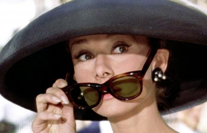 Audrey Hepburn seductively looking over her sunglasses.