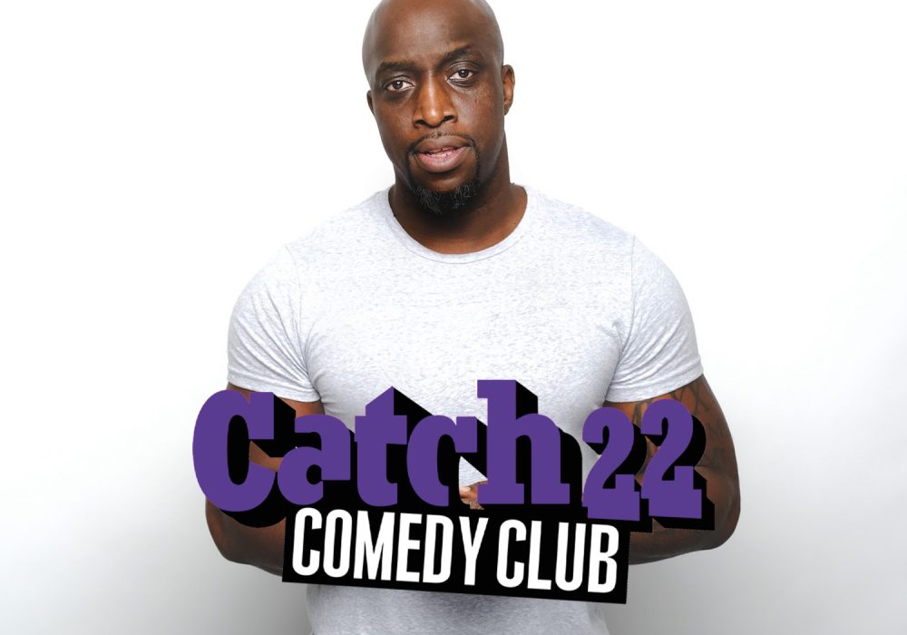 Black male with bald head wearing a white t-shirt. Catch 22 Comedy Club.