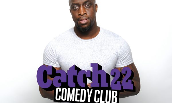 Black male with bald head wearing a white t-shirt. Catch 22 Comedy Club.