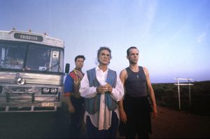 Three individuals stood in front of a bus with the name Priscilla on the front.