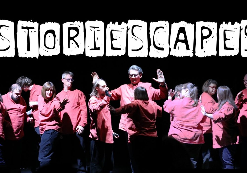 A group of performers in various poses, all wearing matching red shirts, against a plain black background. Text reading 'STORIESCAPES' is overlaid above their heads.