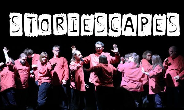 A group of performers in various poses, all wearing matching red shirts, against a plain black background. Text reading 'STORIESCAPES' is overlaid above their heads.