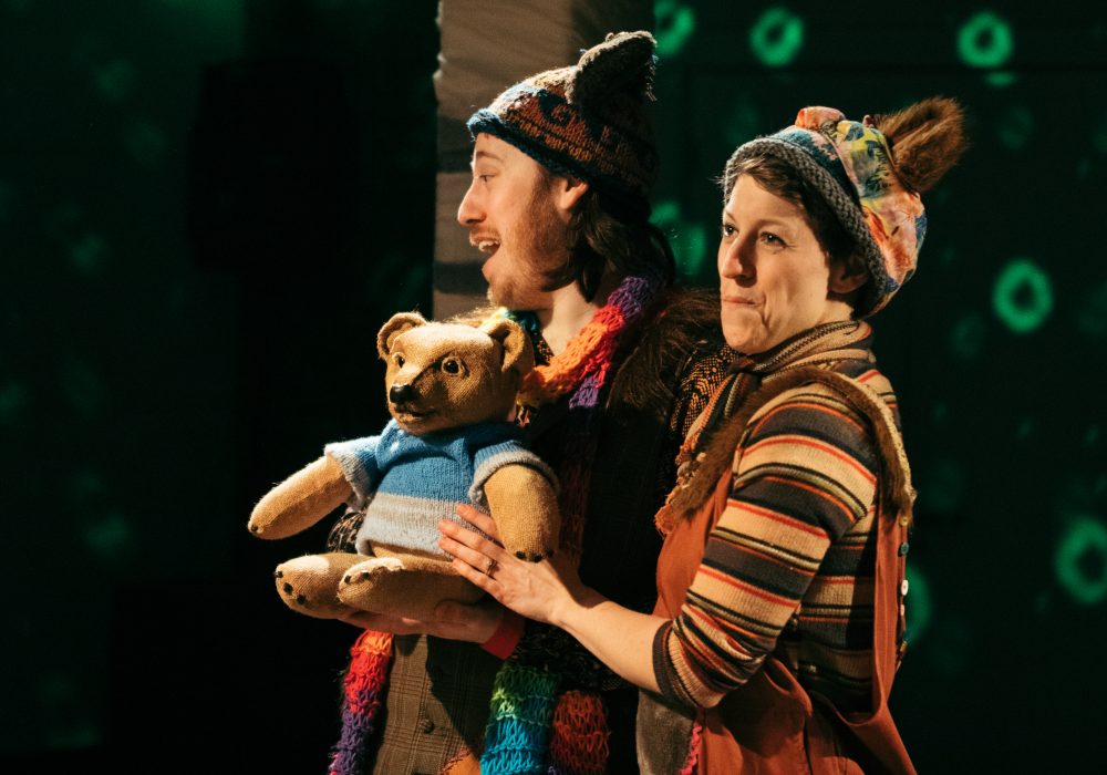 Two performers on stage with a bear puppet