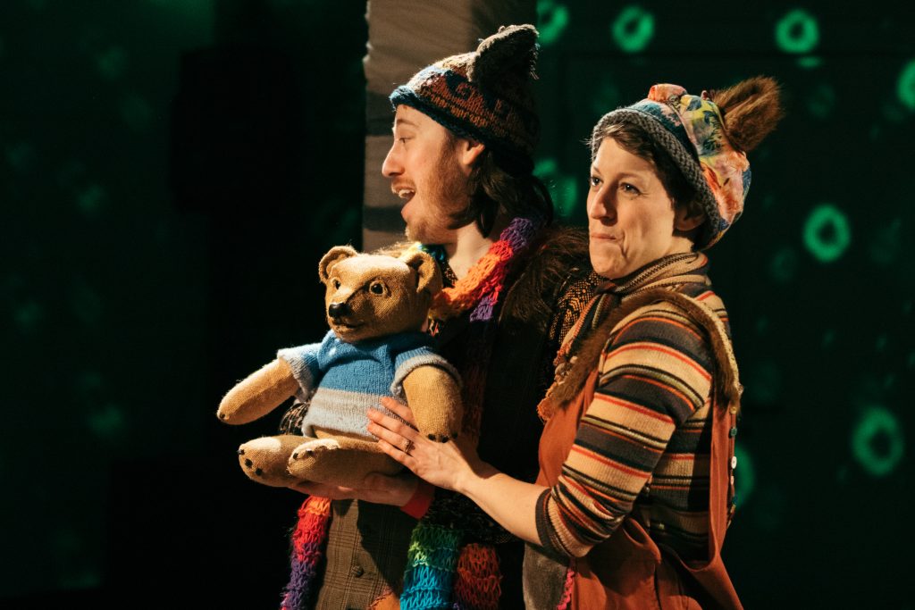 Two performers on stage with a bear puppet