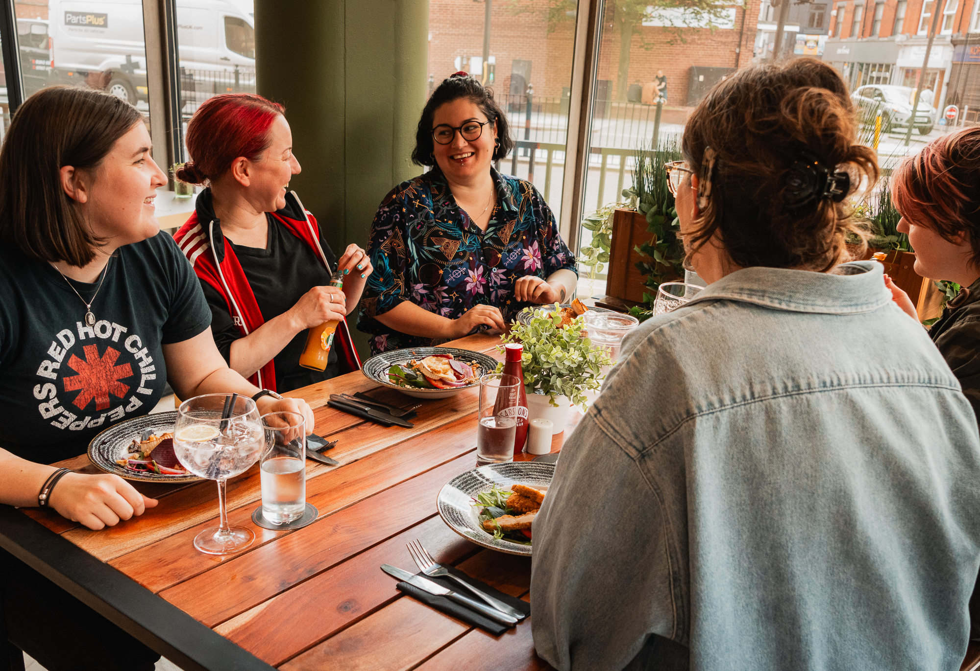 A number of people sit around a wooden table with food and drinks socialising at No 60 ARC's café bar.