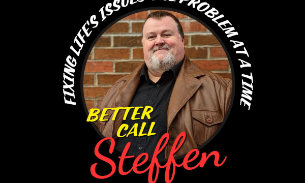 Black background with a circle image of a white male, short dark hair, grey beard, wearing a brown leather jacket and black shirt. He is stood against a brick wall.