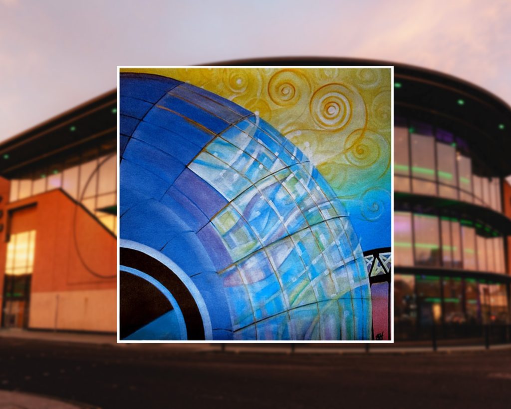 The main focus is a colourful artistic rendering or painting in the foreground. This artwork depicts a large blue curved structure, possibly representing part of a building or architectural element. It has a grid-like pattern of translucent panels, giving it a glass-like appearance. The background of this painting transitions from blue to yellow, with swirling spiral patterns in the yellow area, reminiscent of a stylized sky or abstract design. The background of the overall image shows part of a real building. It appears to be a modern structure with large windows, possibly a commercial or public building. The visible portion is predominantly orange or terracotta in colour, with some green lighting visible.