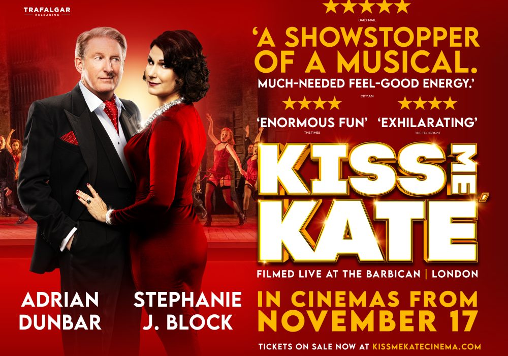 Adrian Dunbar a white male wearing a suit, white shirt, red cravat with Stephanie Block a white femaile with shoulder length dark hair wearing a deep red dress. Kiss Me Kate