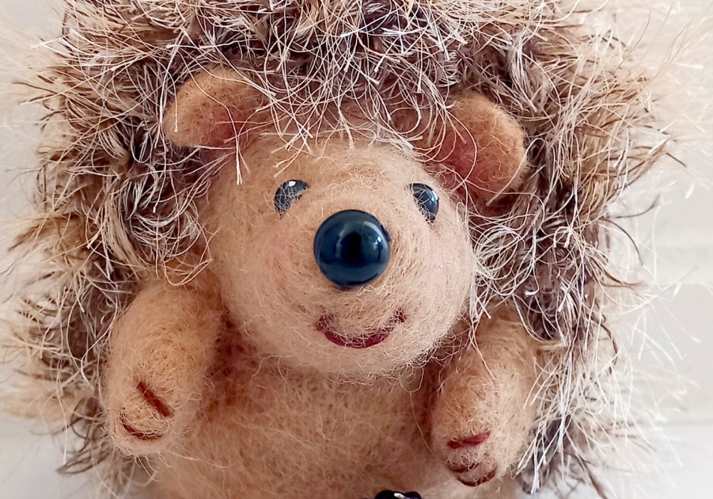 A close up of a needle felt hedgehog, with furry spines and a smiling face,