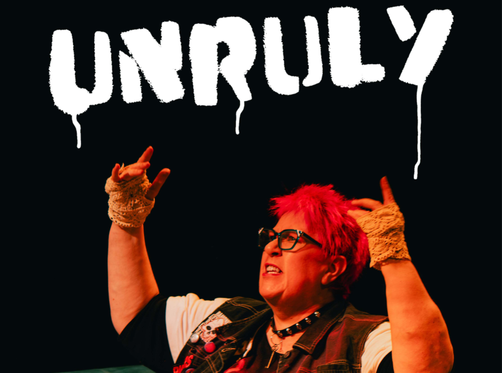 Actress Vici Wreford-Sinnot, with short, bright pink hair, raises her arms up, she has a defiant expression. Above her is the word Unruly, in white spray paint.